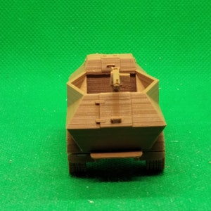 May include: A brown, plastic model of a military armored vehicle with a gun turret on top. The vehicle is on a green background.