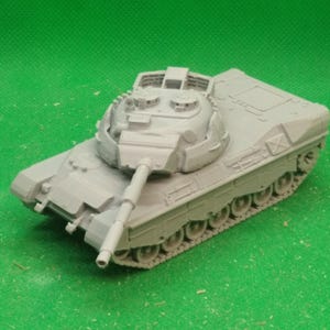 Puede incluir: Un modelo de tanque gris con un cañón largo y orugas detalladas. La torreta del tanque tiene características intrincadas, y el diseño general sugiere un vehículo militar. El modelo está sobre un fondo verde.