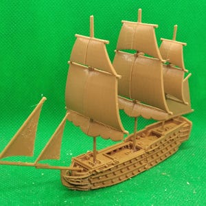 Puede incluir: Un modelo de barco de madera marrón con cuatro velas. Las velas están todas izadas y el barco está sentado sobre una superficie verde.