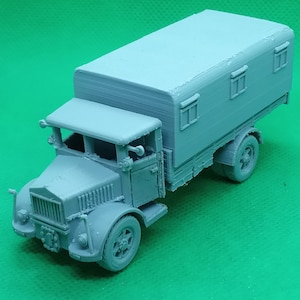 May include: A grey model of a vintage truck with a box body and two windows on the side. The truck has a detailed front grille and headlights.