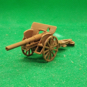 Puede incluir: Un modelo en miniatura de cañón marrón con ruedas de radios y un cañón largo. El modelo está sobre una superficie verde. El cañón tiene un diseño detallado, incluyendo un afuste y un mecanismo de puntería.