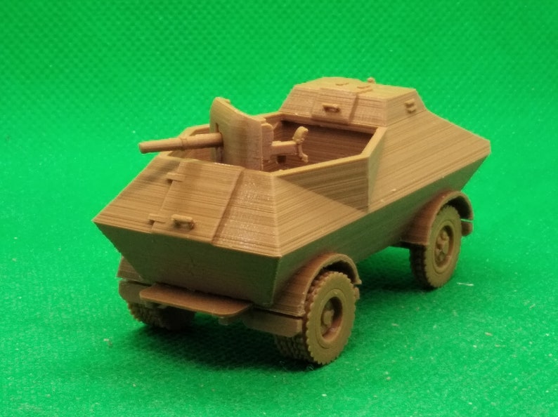 May include: A brown plastic model of a military armored car with a rotating turret and a cannon. The car has four wheels and is on a green surface.