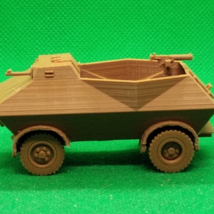 May include: A brown plastic model of a military armored car with a machine gun on top. The car has four wheels and is on a green surface.