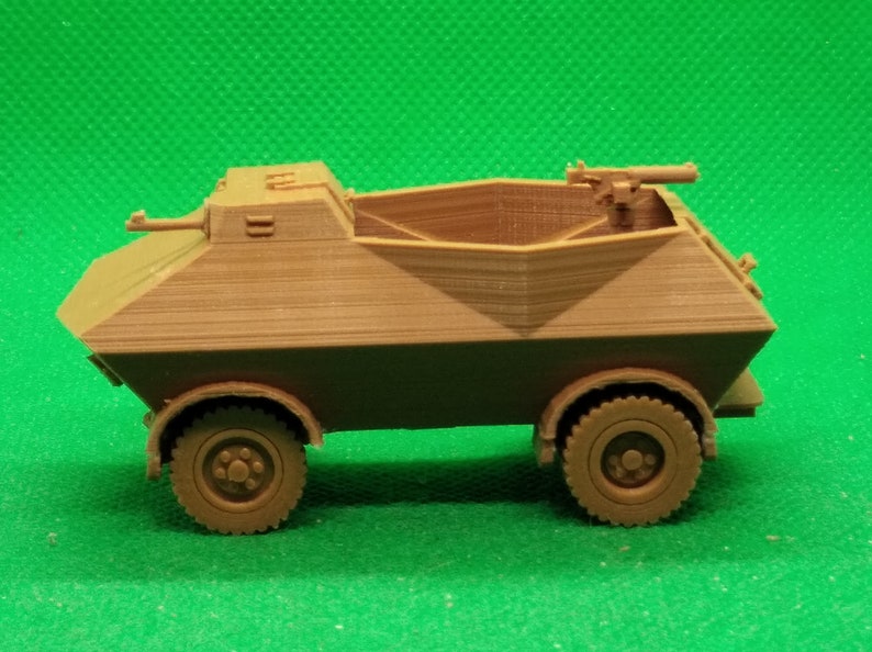 May include: A brown plastic model of a military armored car with a machine gun on top. The car has four wheels and is on a green surface.