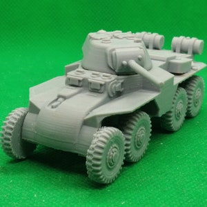 Puede incluir: Un modelo de coche blindado militar de plástico gris con una torreta y una ametralladora. El coche tiene seis ruedas y está sobre una superficie verde.