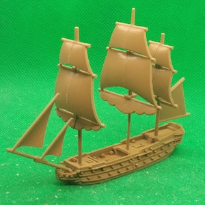 May include: A brown wooden model ship with three sails. The sails are raised and the ship is on a green surface.