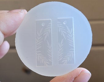 Può includere: Uno stampo in silicone trasparente con due forme rettangolari, ciascuna con un motivo a foglie. Lo stampo è progettato per realizzare orecchini in resina.