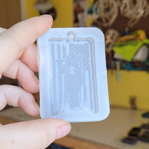 May include: A clear silicone mould for resin casting, featuring a firefighter standing in front of an American flag. The mould is designed to create a keychain or pendant.