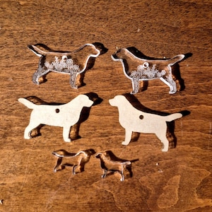May include: Six dog-shaped charms in varying sizes. Two are clear acrylic with white floral line art, two are solid beige opaque material, and two are small clear acrylic silhouettes. Each piece features a small hole for attachment purposes.