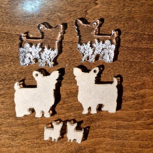 May include: Two clear acrylic dog-shaped charms featuring white floral line art, two solid beige wooden dog-shaped cutouts, and two small beige wooden dog-shaped stud earring components, all arranged in a vertical display.
