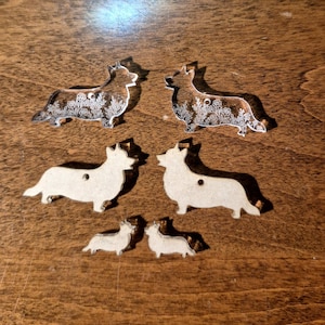 May include: Two clear acrylic Corgi-shaped charms featuring white floral line art, two medium-sized beige Corgi-shaped wooden cutouts, and two small beige Corgi-shaped wooden cutouts, all arranged in three rows on a flat surface.