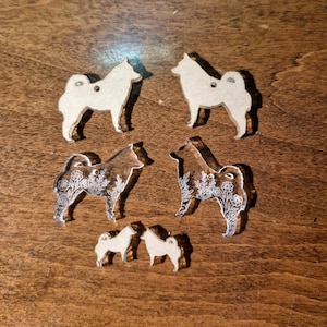 May include: A collection of six dog-shaped charms in three sizes. Two are opaque beige with a small hole, two are clear acrylic with a white floral line art pattern, and two are small opaque beige pieces. All feature a standing dog silhouette.