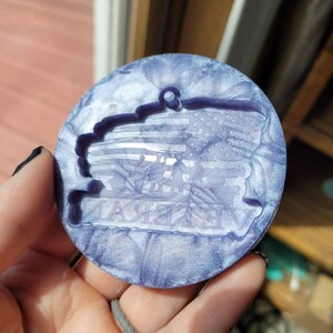 May include: A round, purple and white resin ornament with a raised design of an American flag and the words "Thank You" in a banner.