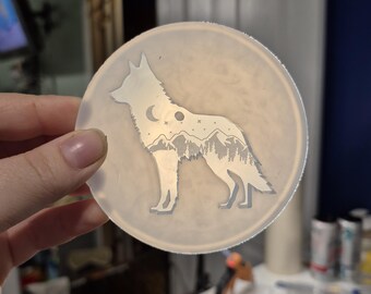 May include: A circular, translucent silicone mold featuring an etched design of a standing wolf. The wolf's body contains a detailed landscape scene with mountain peaks, a forest of pine trees, a crescent moon, and small stars against a clear background.