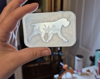 May include: A rectangular, semi-translucent white silicone mold featuring a cutout silhouette of a dog in profile. The interior of the dog shape is filled with intricate, fine-line floral illustrations, including various small flowers and leafy stems.