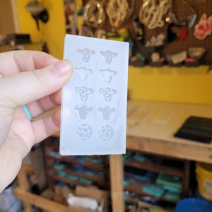 Peut inclure: Un moule en silicone transparent avec huit cavit&eacute;s en forme de vache et deux cavit&eacute;s rondes. Les cavit&eacute;s de vache ont des motifs diff&eacute;rents, notamment une vache avec un bandana, une vache avec des taches et une vache avec un c&oelig;ur. Les cavit&eacute;s rondes sont remplies d'un motif imprim&eacute; vache.