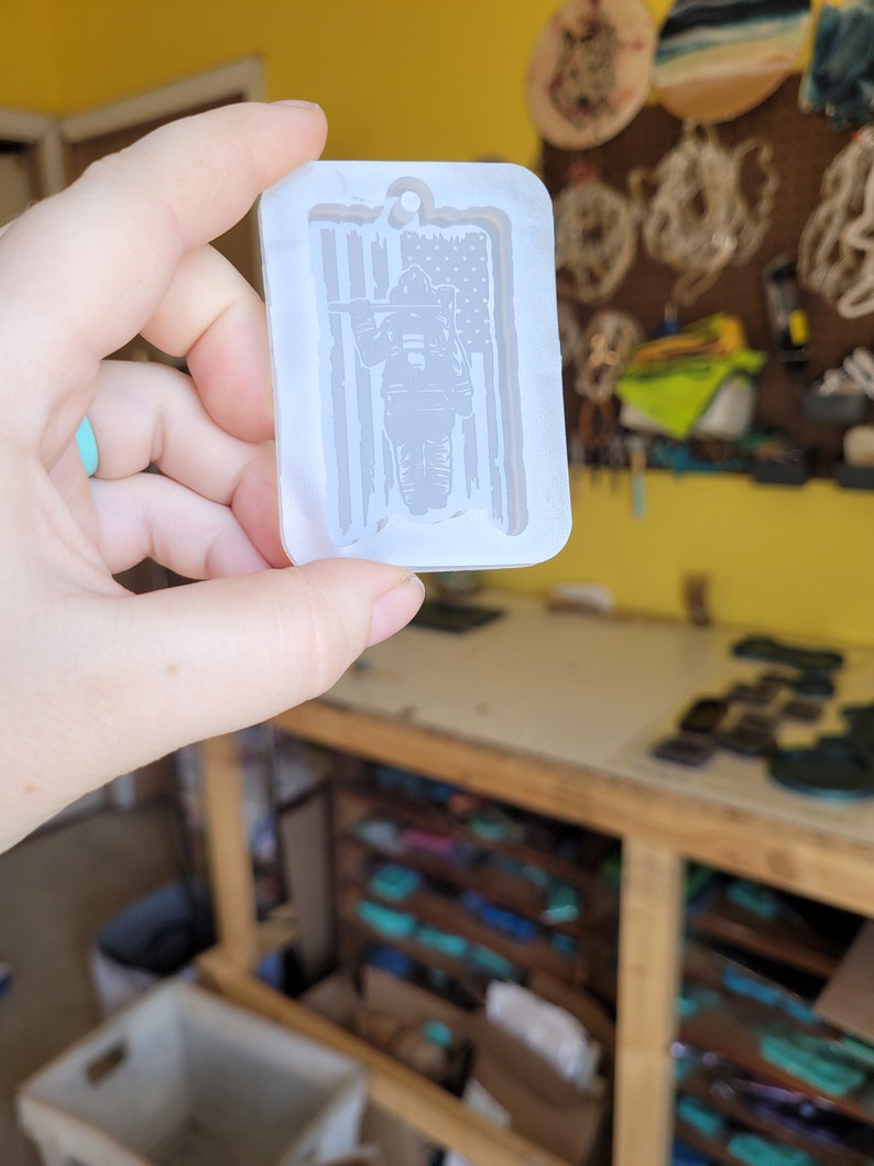 May include: A white silicone mould for making resin crafts. The mould is shaped like a tag and features a firefighter standing in front of an American flag.