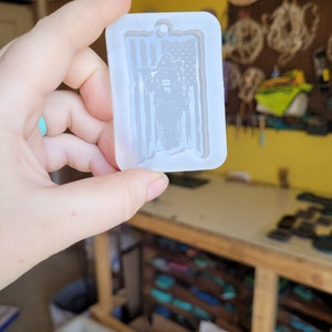 May include: A white silicone mould for making resin crafts. The mould features a firefighter standing in front of an American flag.