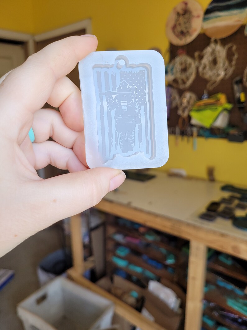 May include: A white silicone mould for making resin crafts. The mould features a firefighter standing in front of an American flag.