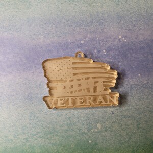 May include: A wooden ornament featuring a distressed American flag design and the word "Veteran" below. The flag has a faded, rustic appearance.