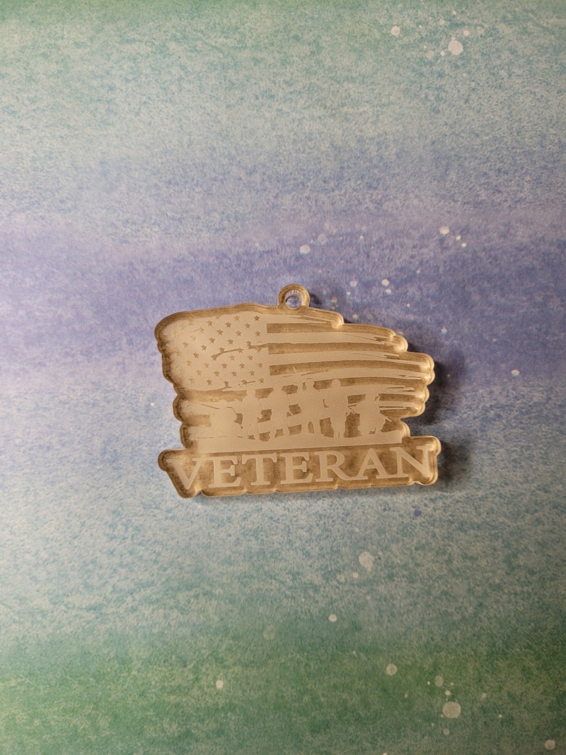 May include: A wooden ornament featuring a distressed American flag design and the word "Veteran" below. The flag has a faded, rustic appearance.