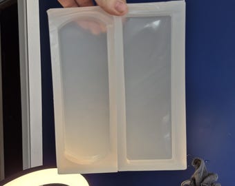 May include: A translucent, rectangular silicone mold featuring two distinct cavities. One cavity has a flat rectangular base, while the other cavity features a rounded, arched top edge. The mold is flexible, clear, and designed for casting crafts.