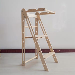 Peut inclure: Une tour d'apprentissage Montessori en bois naturel, avec une conception en forme d'échelle. La tour comprend une plateforme et une barre supérieure pour le soutien. Conçue pour que les enfants atteignent en toute sécurité les surfaces plus hautes. Le bois est clair et non fini.