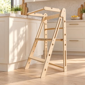May include: A light-coloured wooden learning tower featuring a two-step design with side support rails and a top safety bar. The structure is constructed from plywood with visible circular cutouts along the side frames and metal hardware.
