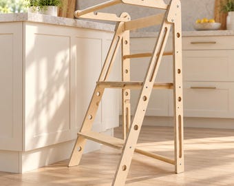Puede incluir: Una torre de aprendizaje de madera clara con un diseño de dos escalones, rieles de soporte laterales y una barra de seguridad superior. La estructura está hecha de madera contrachapada con recortes circulares en los laterales.