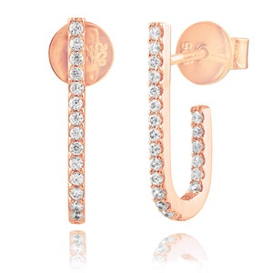 May include: A pair of rose gold earrings with a minimalist design. Each earring features a thin, curved bar with a row of small, clear cubic zirconia stones.