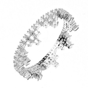 May include: A silver ring with a delicate design of small, clear stones set in a band that is shaped like a crown.