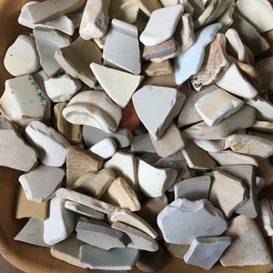 May include: A wooden bowl filled with a variety of broken white, tan, and gray ceramic pieces.