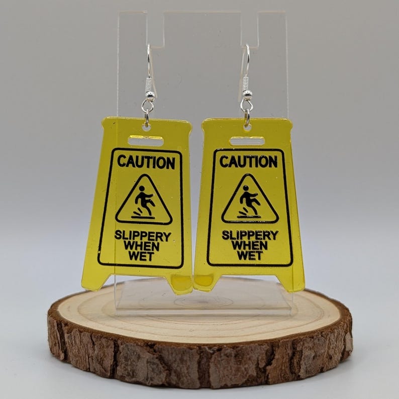 May include: A pair of yellow caution sign earrings with the text "CAUTION SLIPPERY WHEN WET" and a black silhouette of a person slipping.
