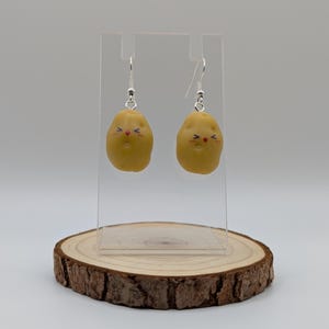 May include: A pair of dangle earrings featuring a cute potato design with a smiling face. The earrings are made of polymer clay and have silver hooks.