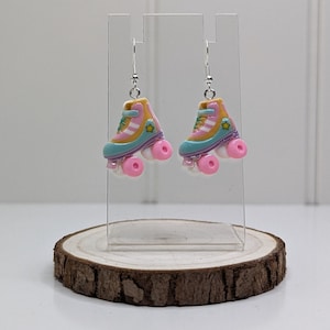 May include: A pair of silver roller skate earrings with pink, blue and yellow details. The skates have a yellow star on the side.