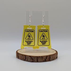 May include: A pair of yellow caution sign earrings with the text "CAUTION" and "SLIPPERY WHEN WET".