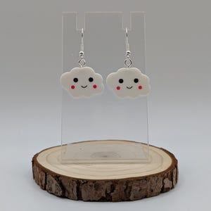 May include: White cloud shaped earrings with a smiling face and red cheeks. The earrings are hanging from silver hooks.