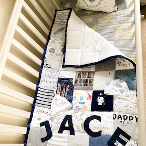 Może przedstawiać: Kołdra patchworkowa wykonana z ubranek dla niemowląt z imieniem "Jace" napisanym dużymi czarnymi literami. Kołdra jest wykonana z różnych tkanin, w tym niebieskiego, szarego i białego. Kołdra jest otoczona białym łóżeczkiem.