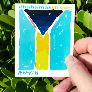 May include: A sticker with the Bahamian flag, featuring a black triangle with a blue center, a yellow stripe, and a turquoise background. The text "#bahamasstrong" and "A+A Kiki" are printed on the sticker.