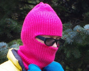 Puede incluir: Una balaclava de punto rosa con agujeros para los ojos y unas gafas de sol negras.
