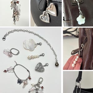 May include: A collection of silver-toned bag charms and accessories. The charms include heart-shaped lockets, pearl strands, butterfly and flower pendants, and a keychain with beads and charms. These accessories are designed to be attached to handbags.