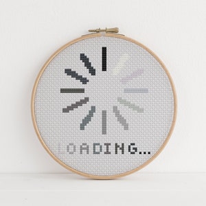 May include: A white embroidery hoop with a black and gray loading symbol and the text "LOADING..." embroidered on it.