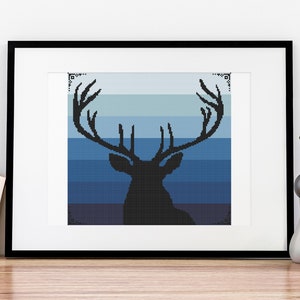 May include: A framed print of a black silhouette of a deer with antlers against a blue and gray ombre background.