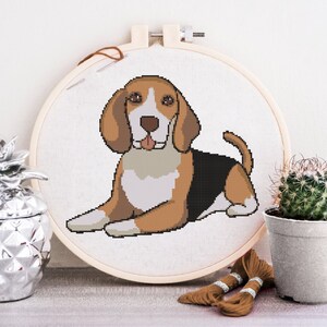 Puede incluir: Aro de bordado de punto de cruz con un diseño de perro beagle marrón, negro y blanco. El perro está sentado con la lengua fuera.
