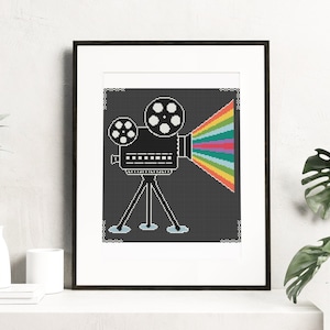 May include: A black and white illustration of a vintage movie projector with a rainbow beam of light coming from the lens. The projector is on a tripod and is set against a dark grey background.