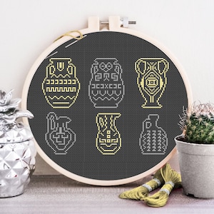 May include: A black embroidery hoop with a design of six yellow Greek amphorae on a black background. The hoop is surrounded by a pineapple, a cactus, and yellow embroidery floss.