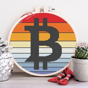 May include: A round embroidery hoop with a retro-style sunset design featuring a black Bitcoin symbol. The hoop is surrounded by red embroidery floss and a silver pineapple.