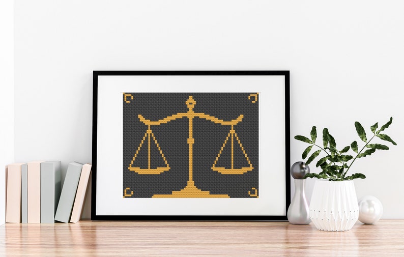 May include: A framed cross-stitch design of a gold scale on a black background. The scale is a symbol of justice and balance.