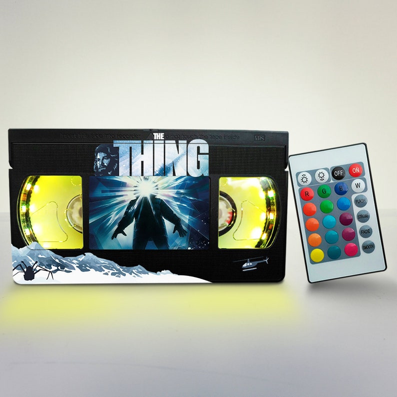 Puede incluir: Una l&aacute;mpara negra en forma de cinta VHS con una luz LED de cambio de color. La parte frontal de la l&aacute;mpara presenta una escena de la pel&iacute;cula "The Thing" con el texto del t&iacute;tulo. La l&aacute;mpara viene con un mando a distancia para cambiar los colores de la luz.