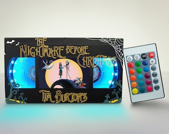 May include: A black and white VHS tape-shaped light with a scene from the movie "The Nightmare Before Christmas" on the screen. The light is illuminated with blue light and comes with a remote control to change the color of the light.